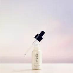 Dropper bottle of skincare serum on a glossy white surface with a soft pastel pink and blue background, ready for use.