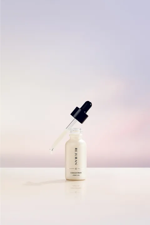 Dropper bottle of skincare serum on a glossy white surface with a soft pastel pink and blue background, ready for use.