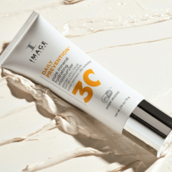 Tube labeled 'Daily Prevention' mineral sunscreen moisturizer SPF 30 lying on a creamy surface nearby splashes of product.