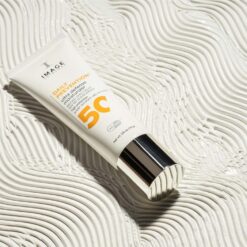 Tube of sunscreen labeled SPF 50+ rests on a ridged white surface on a sunlit background that highlights its labeling.