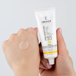 White tube of IMAGE Skincare Prevention SPF 30 sunscreen held over a hand, with a small dab of clear gel on the back of the hand used for demonstration.
