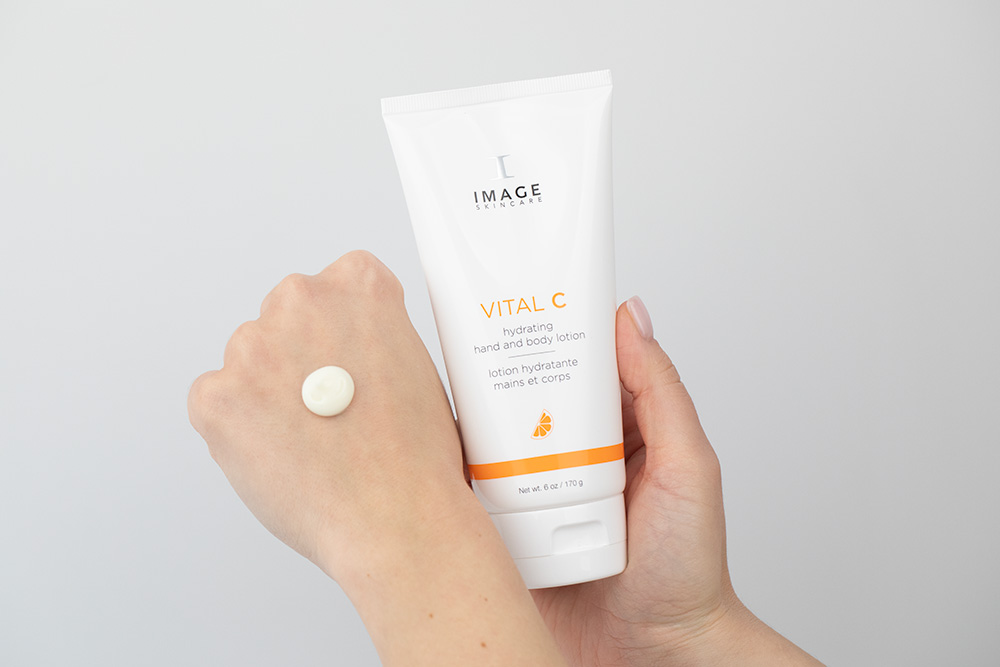 Tube of Image Skincare Vital C hydrating hand and body lotion held in one hand, with a dollop of lotion on the back of the other hand
