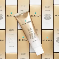 Tube of REJURAN Active Cream Enhanced c-PDRN 0.2% lies diagonally on stacked beige and white boxes with the logo visible.
