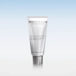 Silver skincare tube with INSTYTUTUM branding on a reflective surface against a blue gradient background, product displayed upright.