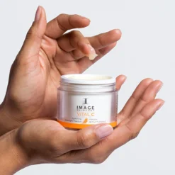 Hands cradle a jar of Image Skincare Vital C hydrating overnight masque with a small dab of product on the finger.